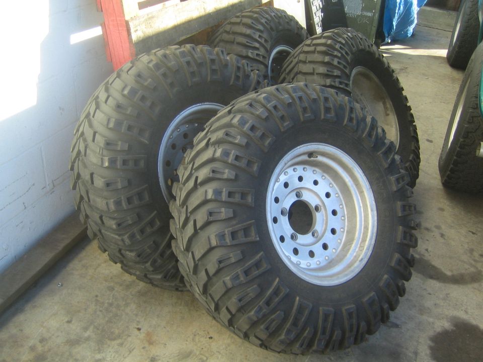Four mud-terrain tires on silver aluminum wheels in a garage