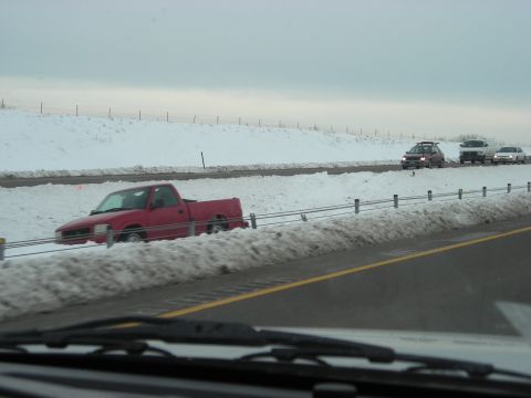 2002 Ford Excursion - A red pickup truck is partially stuck in snow on the side of a highway, with other vehicles driving past.