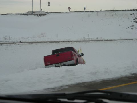 2002 Ford Excursion - A red pickup truck is stuck in a snowdrift on the side of a highway.