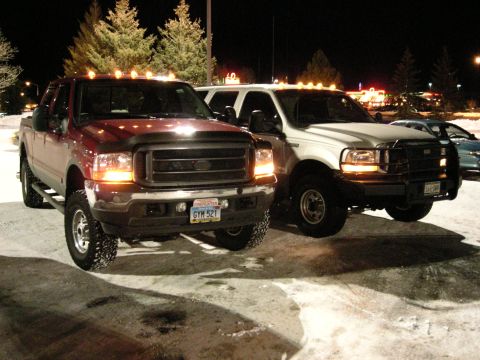 2002 Ford Excursion - Two Ford Super Duty trucks are parked in the snow at night. The red truck in front has a license plate GYM 521.