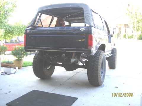 1994 Ford Bronco - Rear view of a black SUV with a soft top and lifted suspension, parked outdoors.