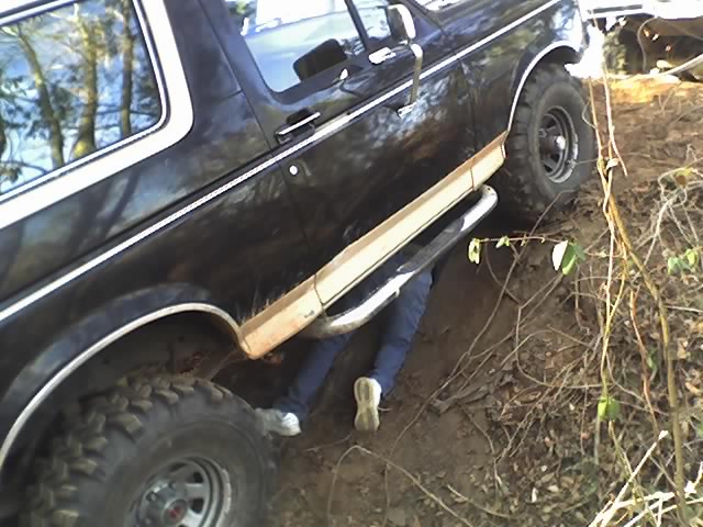 Person lying under a black Bronco on an off-road trail working on the truck