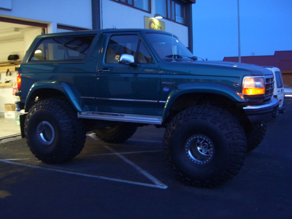 Teal lifted two-door Ford Bronco on large off-road tires, 3/4 front view at dusk