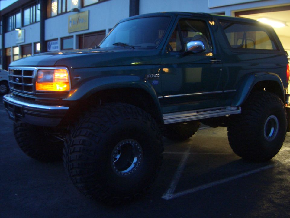 Dark green lifted two-door Ford Bronco on large off-road tires, front 3/4 view at dusk