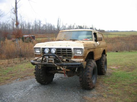 1992 Ford Mustang - A heavily modified tan Ford Bronco sits on a gravel road, covered in mud.
