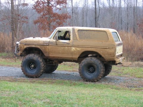 1992 Ford Mustang - This heavily modified SUV, covered in mud, sits off-road with its large tires visible.