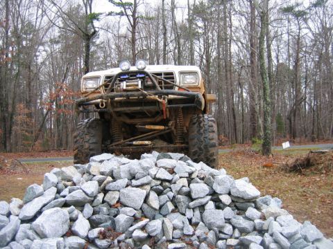 1992 Ford Mustang - A heavily modified off-road vehicle sits in a wooded area, positioned in front of a large pile of gray rocks.