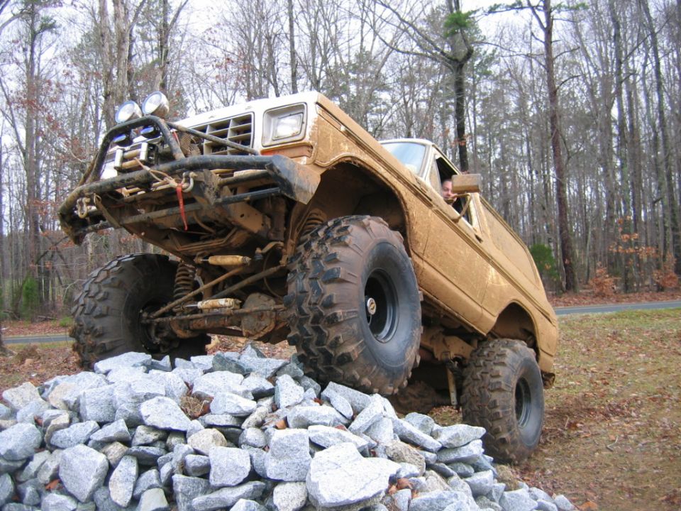 Brown off-road SUV with large tires climbing over rocks, front grille and headlights visible