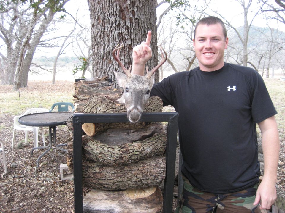 Man with deer head mounted on logs, pointing up with finger
