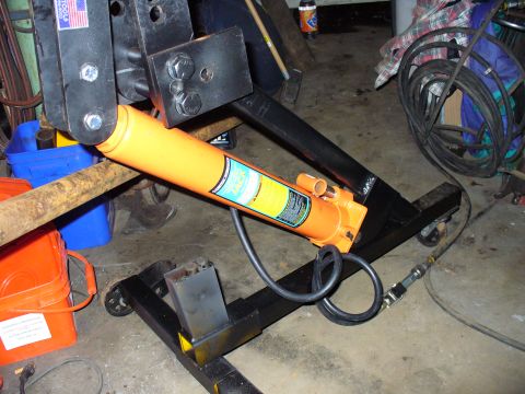 1978 Ford Bronco - A hydraulic ram is mounted on a wheeled stand, with a rusty bar nearby. The scene appears to be a workshop or garage.