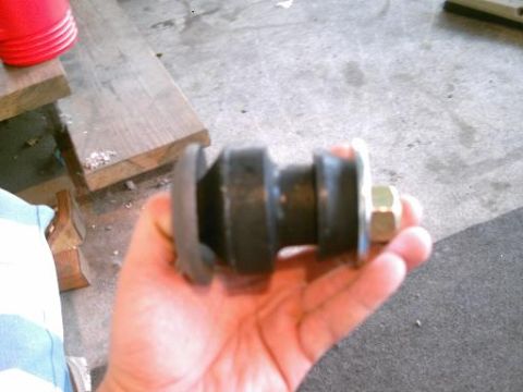 1986 Ford Bronco - A suspension bushing with a bolt is held in a hand, with wooden planks and concrete floor in the background.