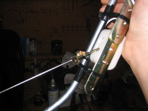 1979 Ford Bronco - A hand holds a zinc-plated fuel sending unit assembly over a workbench, showing the white plastic float, bent metal pickup tube and float a…
