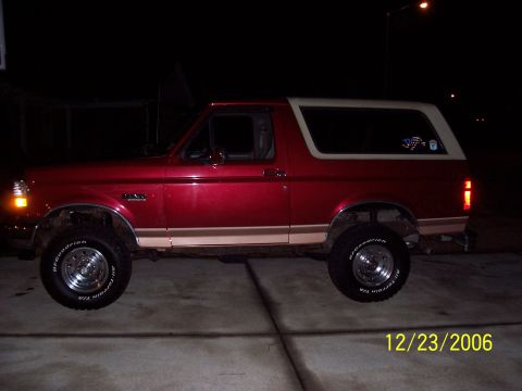 1994 Ford Bronco - A red 1994 Ford Bronco is shown parked on a concrete surface at night, a lifted suspension and off-road tires.
