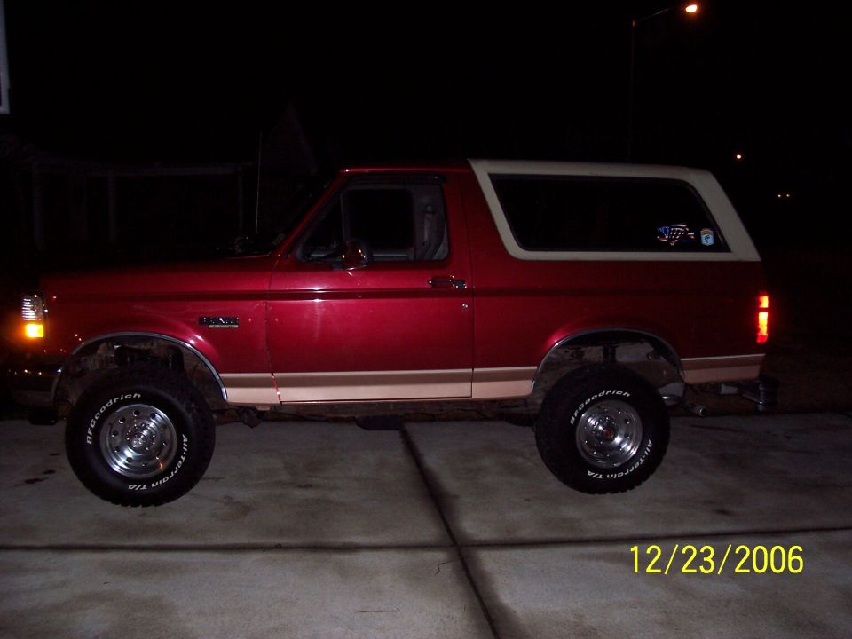 Red full-size Ford Bronco with tan top, lifted, at night