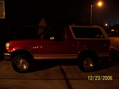 1994 Ford Bronco - This red Ford Bronco with a white top is viewed from the side at night.