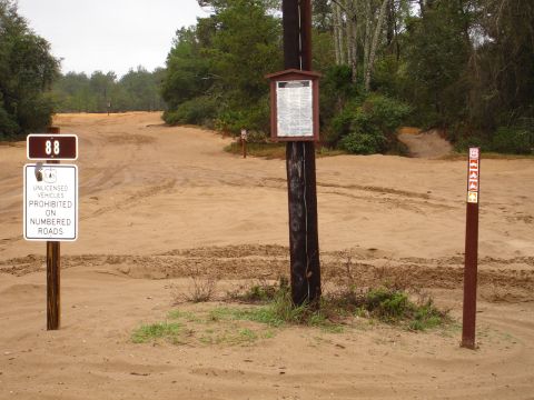 1989 Ford Bronco - A sandy off-road area with signage indicating restrictions for unlicensed vehicles on numbered roads.