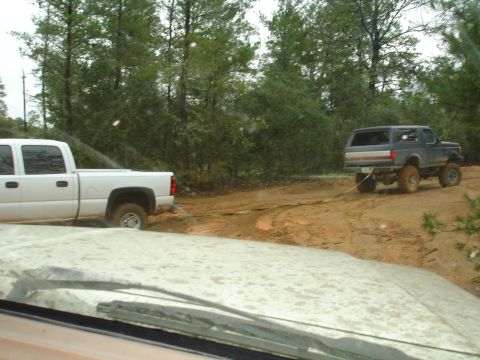 1989 Ford Bronco - A 1989 Ford Bronco is being towed by a white pickup truck through a muddy, wooded area.