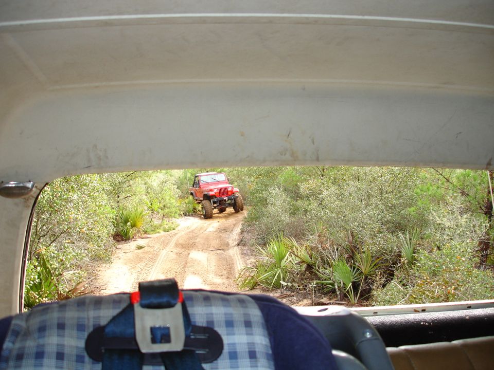 Red off-road vehicle on a dirt path surrounded by brush