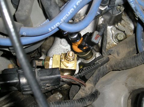 1993 Ford Bronco - This image shows a close-up view of engine components, specifically a fuel injector and a brass sensor, with associated wiring and hoses.