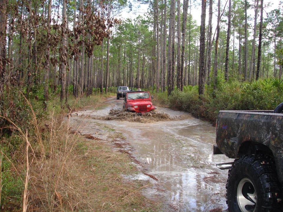 Red Jeep Wrangler splashing through mud on a wooded trail