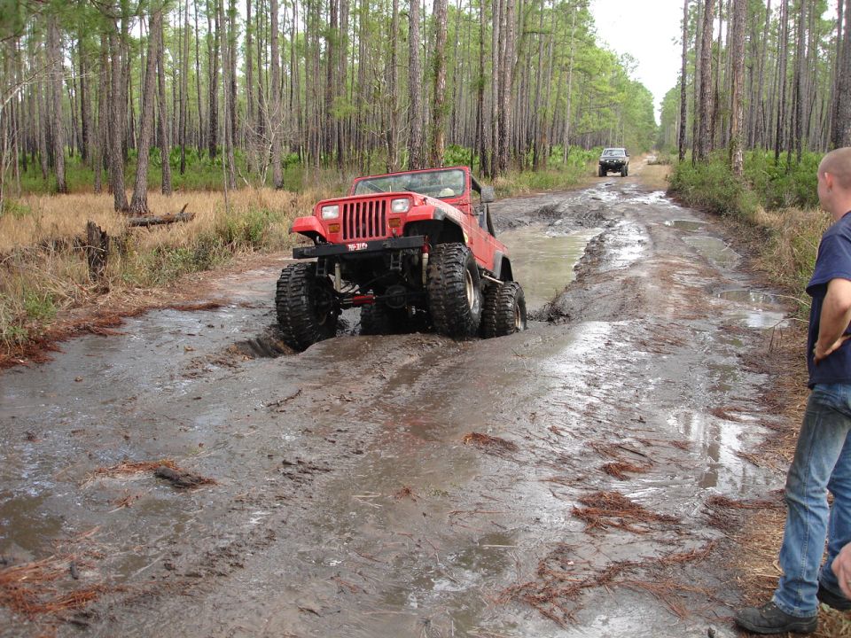 Red Jeep stuck in mud on a forest trail with another vehicle behind