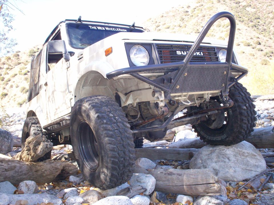White 1987 Suzuki Samurai with large tires navigating rocky terrain