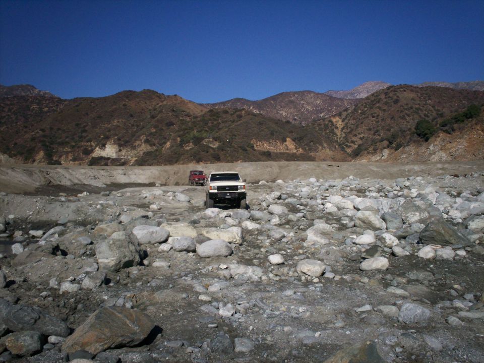 White off-road vehicle and red off-road vehicle on rocky terrain with mountains in background