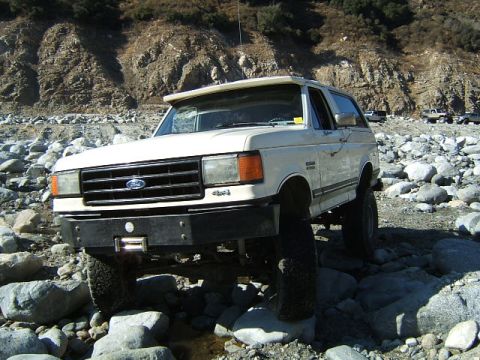 1988 Ford Bronco - A white Ford Bronco navigates a rocky terrain, with other vehicles visible in the distance.