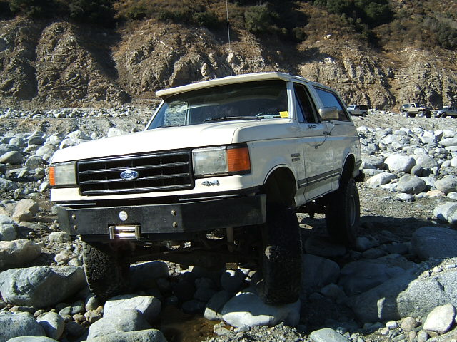 White Ford Bronco on rocks, winch on bumper. Other vehicles in background
