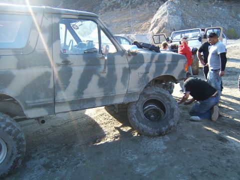 1988 Ford Bronco - A group of people are gathered around a Ford Bronco that appears to have a flat tire, with another vehicle in the background.