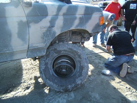1988 Ford Bronco - A group of people gather around a camouflaged Ford Bronco with a flat tire.