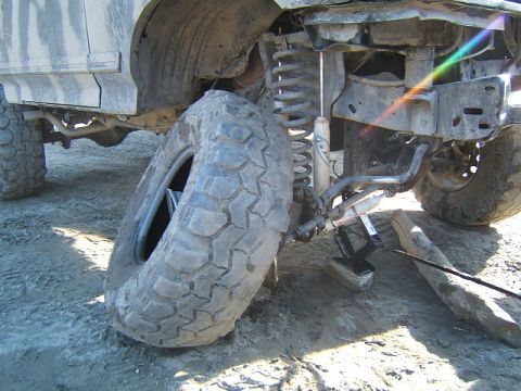 1988 Ford Bronco - A flat tire is shown on a 1988 Ford Bronco, with the vehicle's suspension and undercarriage exposed.