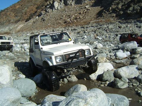 1988 Ford Bronco - Multiple off-road vehicles traverse a rocky, water-filled terrain under a clear sky.
