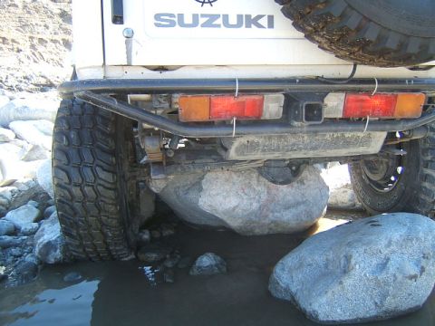 1988 Ford Bronco - This Suzuki Samurai is navigating rough terrain, with its rear tire and bumper clearly visible as it's caught on large rocks in shallow wat…