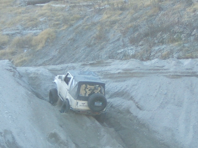 White off-road vehicle with soft top and spare tire on a dirt slope