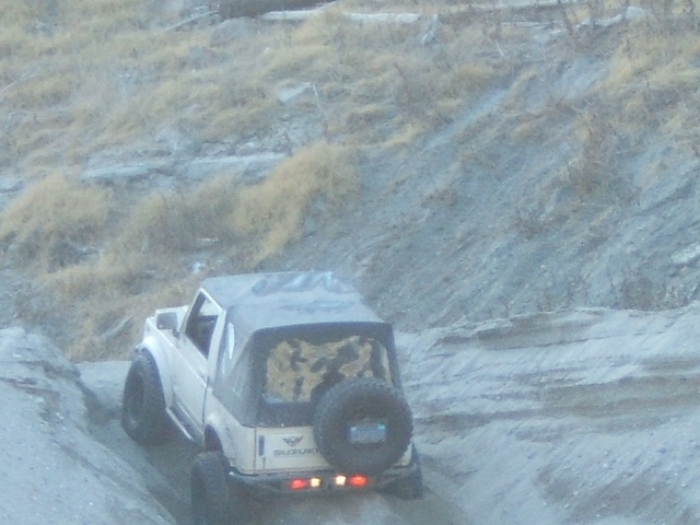 Suzuki Samurai with soft top and spare tire on rear, driving up a dirt incline