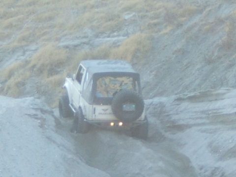 1988 Ford Bronco - A white Suzuki Samurai navigates a dusty, off-road trail with a spare tire on the rear.