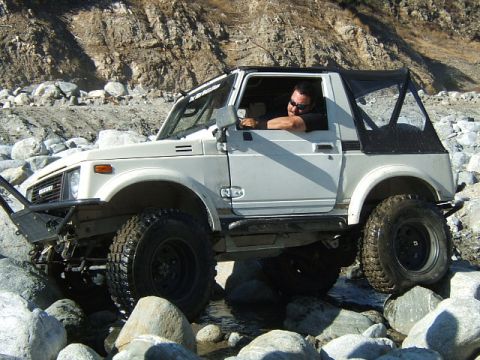 1988 Ford Bronco - A white Suzuki Samurai is shown off-roading through a rocky stream bed.