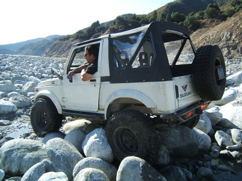 1988 Ford Bronco - Suzuki Samurai off-roading over large rocks in a dry riverbed.