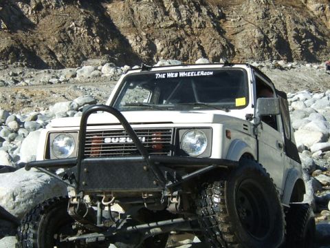 1988 Ford Bronco - Suzuki Samurai tackles a rocky trail, its off-road capabilities with a prominent aftermarket bumper and a website sticker on the windshield.
