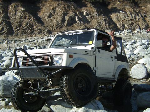 1988 Ford Bronco - Suzuki Samurai tackles a challenging rocky riverbed, driver waves from the window.