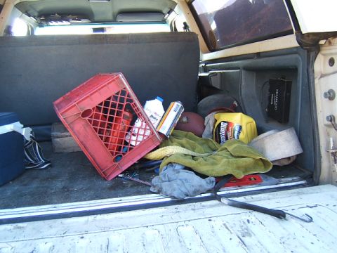 1988 Ford Bronco - The cargo area of a vehicle is filled with various items, including a red milk crate and a yellow jug of oil.