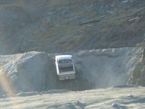 1988 Ford Bronco - A silver pickup truck is seen from the rear, descending into a sandy pit.