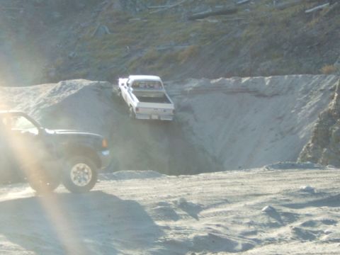 1988 Ford Bronco - Two trucks navigate a sandy incline in an off-road setting.