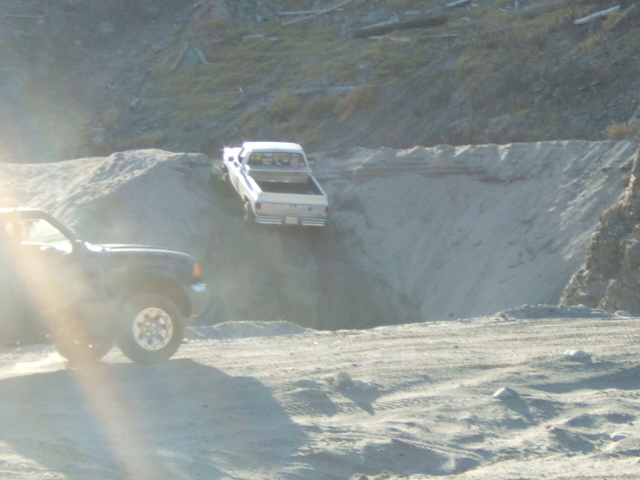 Two trucks on a sandy slope, one is white and going down, the other is dark and in the foreground