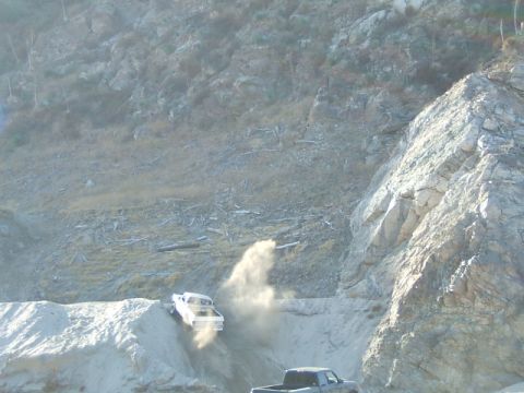 1988 Ford Bronco - A white pickup truck navigates a steep, dusty incline, with another vehicle visible in the foreground.