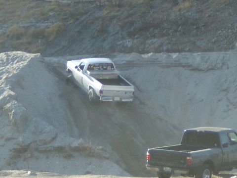 1988 Ford Bronco - Two pickup trucks are seen in a sandy, hilly terrain.