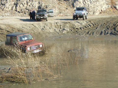 1988 Ford Bronco - Multiple off-road vehicles navigate a muddy terrain with water obstacles.