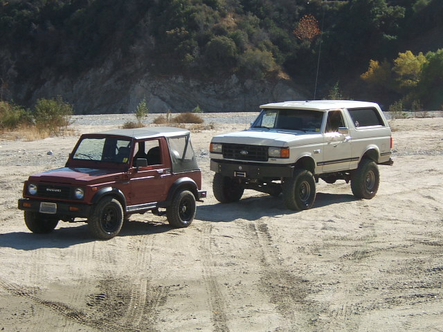 White Ford Bronco and red Suzuki Samurai parked on dirt road