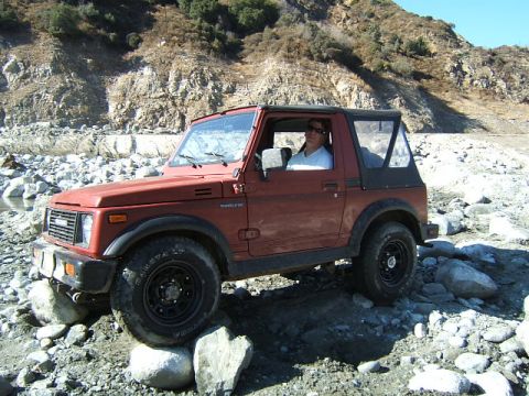 1988 Ford Bronco - A red Suzuki Samurai navigates a rocky, off-road path, demonstrating its capabilities.